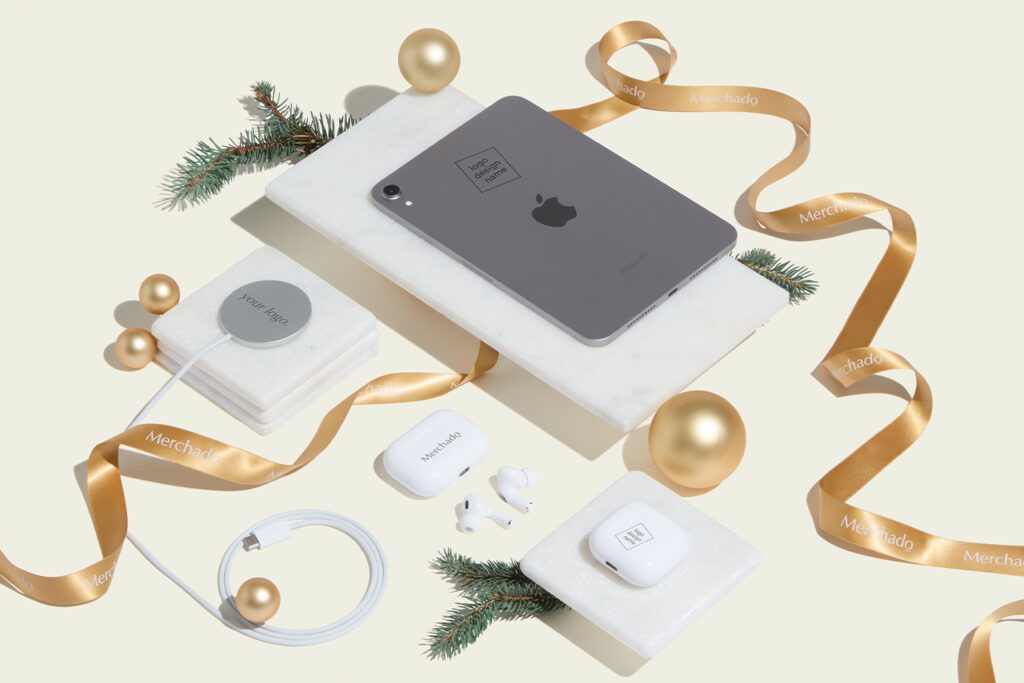 Sfeerbeeld van gepersonaliseerde Apple producten voor de feestdagen, waaronder een iPad mini, AirPods en MagSafe oplader tussen kerstversiering