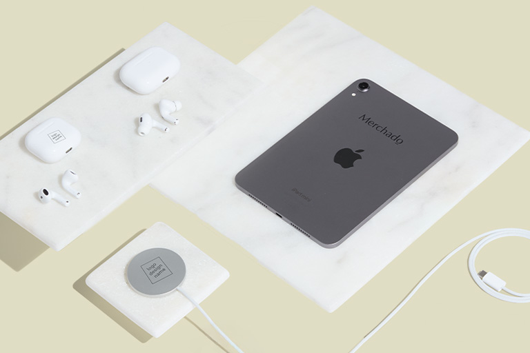 Overhead shot van een grijze iPad mini met 'Merchado' logo, twee sets AirPods en een MagSafe oplader op marmeren blokken, representatief voor premium Apple corporate gifts
